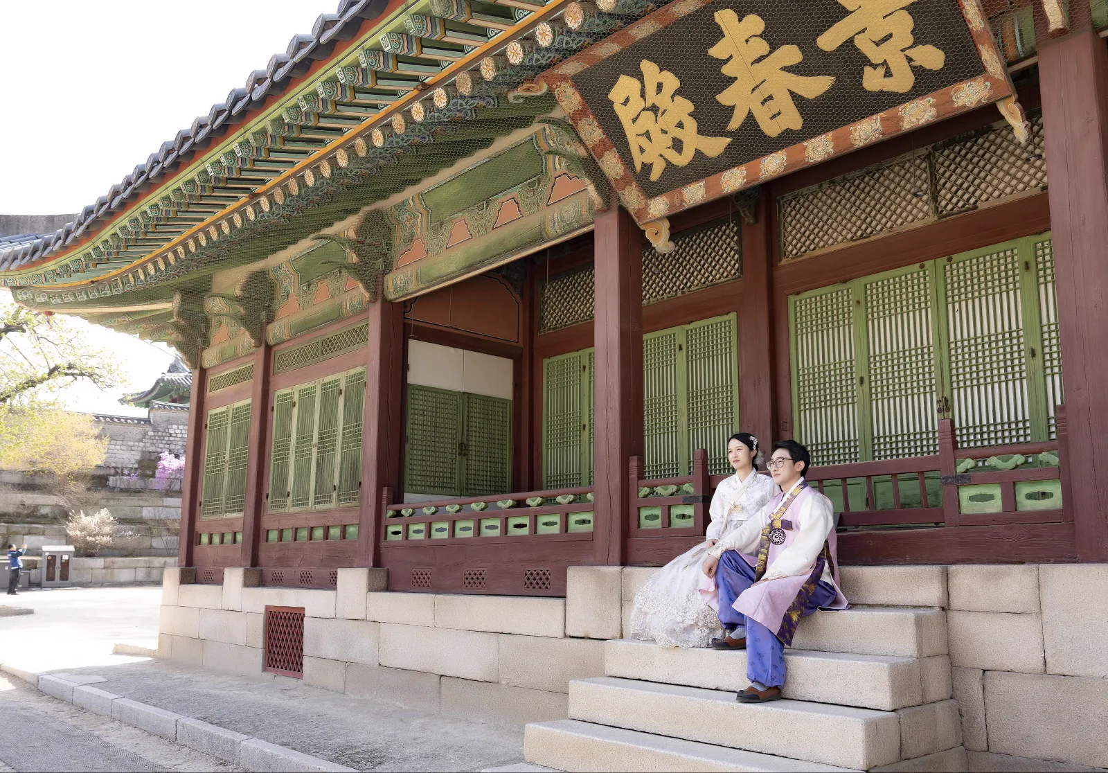 A wide couple portrait showing the traditional architecture of Changgyeonggung Palace
