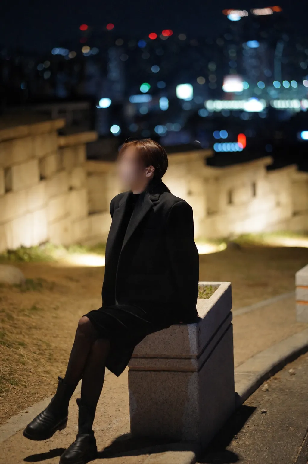 A privacy-blurred night portrait beside the illuminated Seoul City Wall at Naksan Park