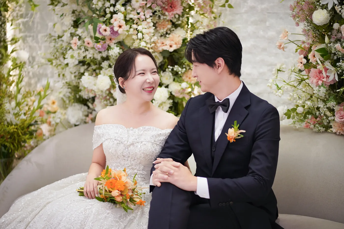 소파에 나란히 앉아 마주 보며 웃는 신랑 신부