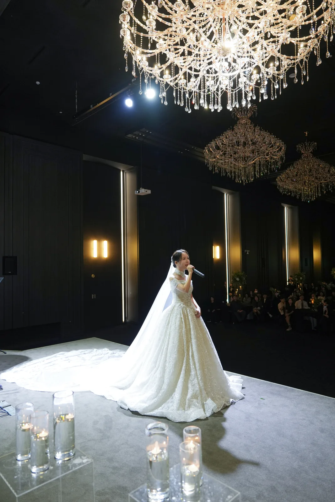 A bride standing in a spotlight in an otherwise dark ceremony hall