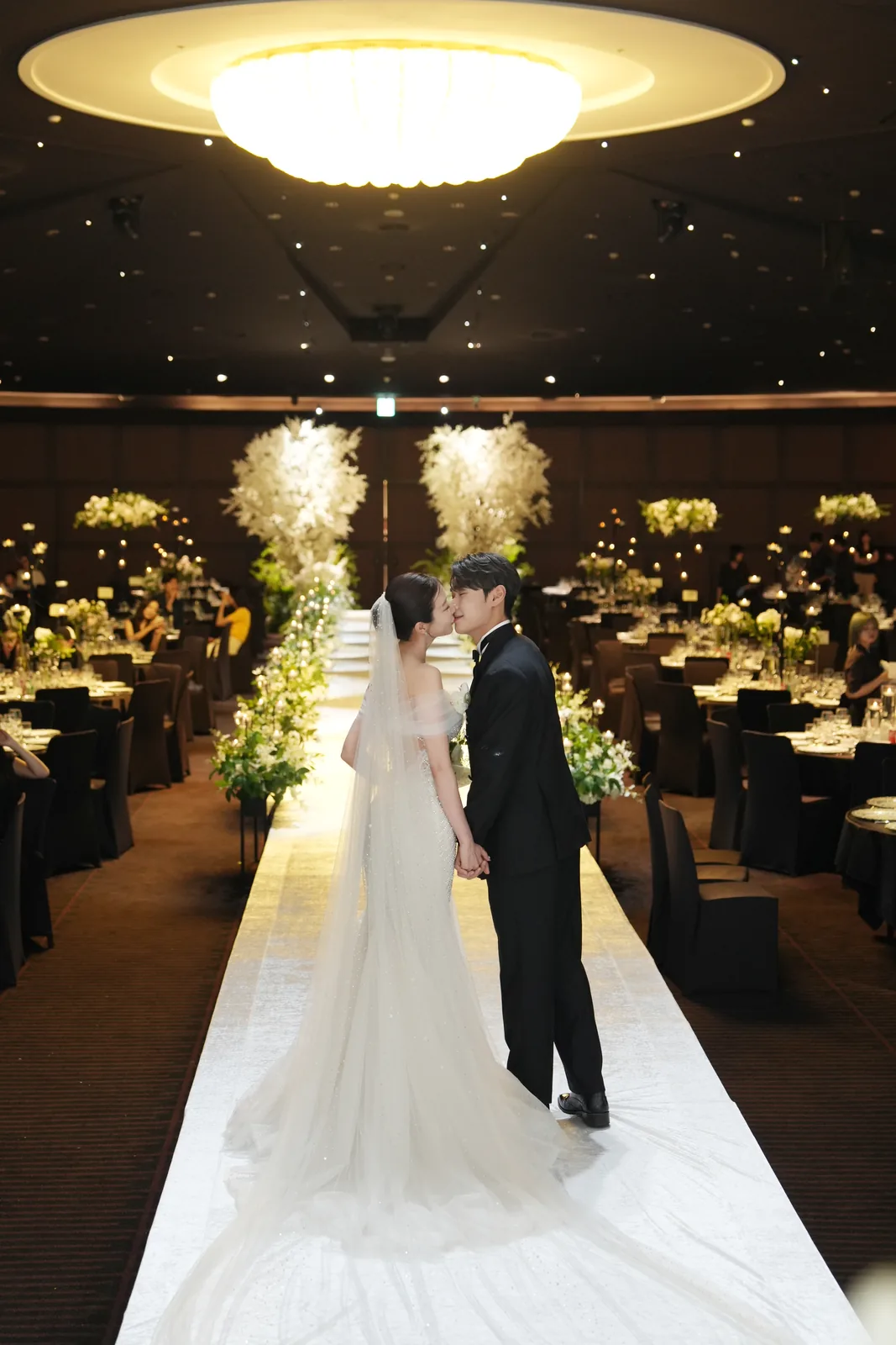 A couple facing each other in a hotel ballroom with light laid along the aisle